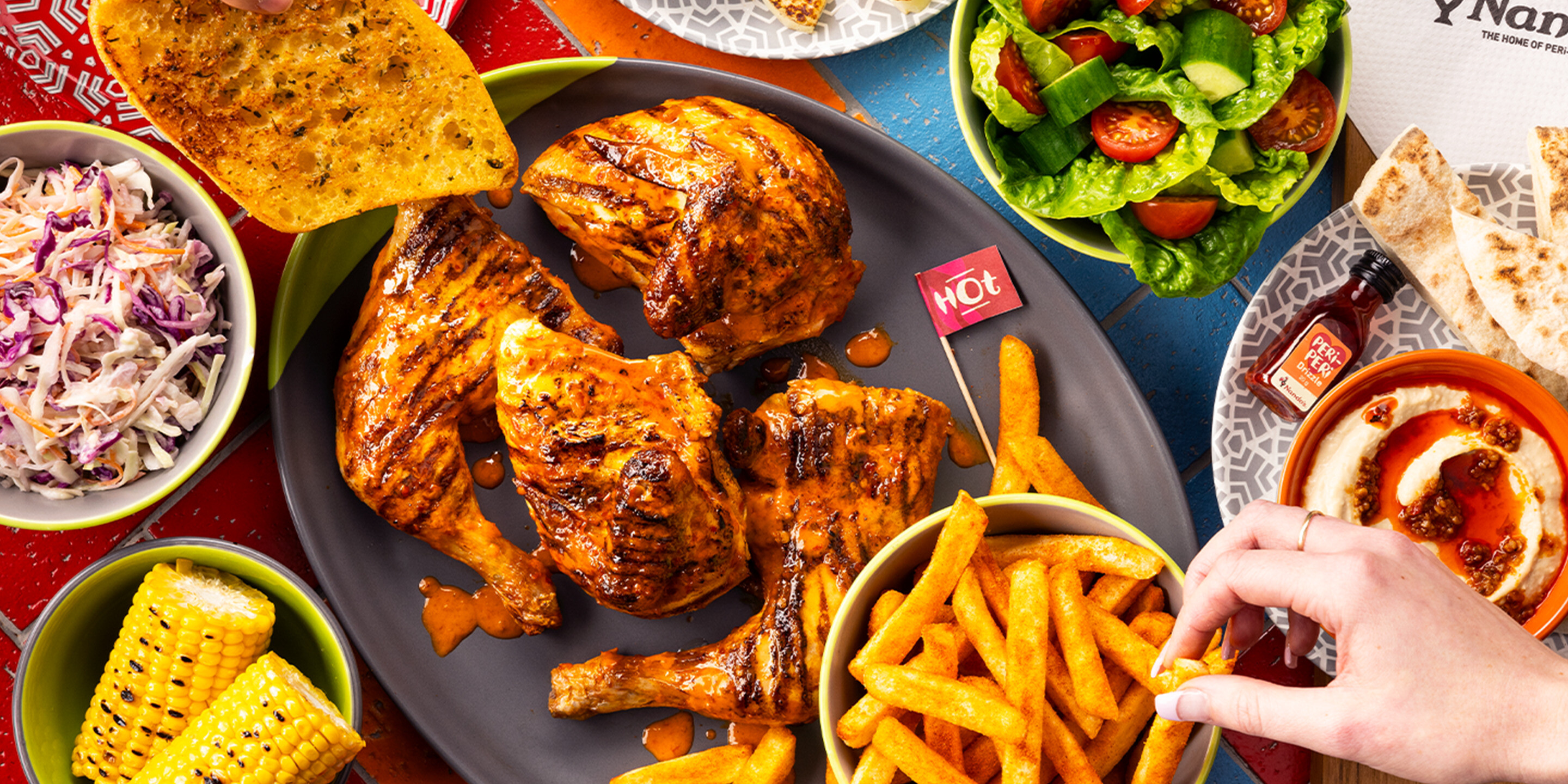 a Nando’s meal on a table including PERi-PERi chicken, a salad, chips, and a selection of sides